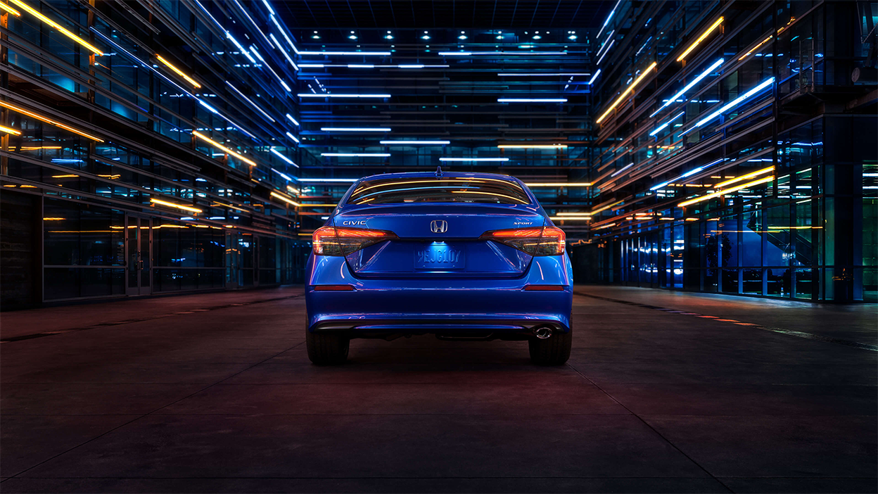 Arrière d’une Civic berline bleue stationnée dans un espace sombre comme un entrepôt.